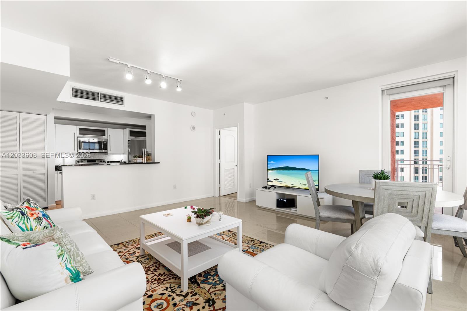 A living room features white furniture, a patterned rug, and a kitchen pass-through window — 7350 SW 89th St # 1610S, Miami FL 33156, MIAMI, FL