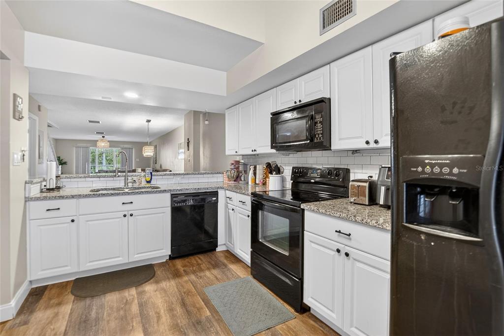 A kitchen with white cabinets, black appliances, and granite countertops overlooks an open living area — 2599 DOLLY BAY DRIVE UNIT 305, PALM HARBOR, FL