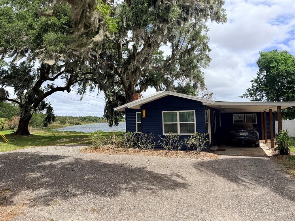 A blue house with a carport sits on a gravel lot near a lake — 915 W MAIN STREET, LAKE HAMILTON, FL