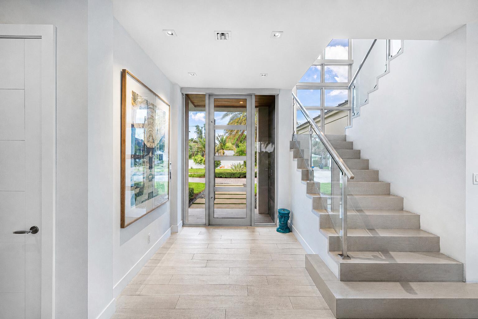 A bright entryway features light tile flooring, a glass front door, and a floating staircase — 1508 Lake Drive, Delray Beach FL 33444, DELRAY BEACH, FL