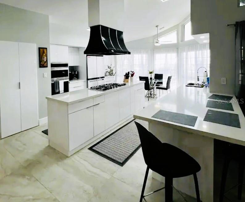 A modern white kitchen features a large island, black range hood, and tile flooring — 15618 SE US HIGHWAY 301, HAWTHORNE, FL