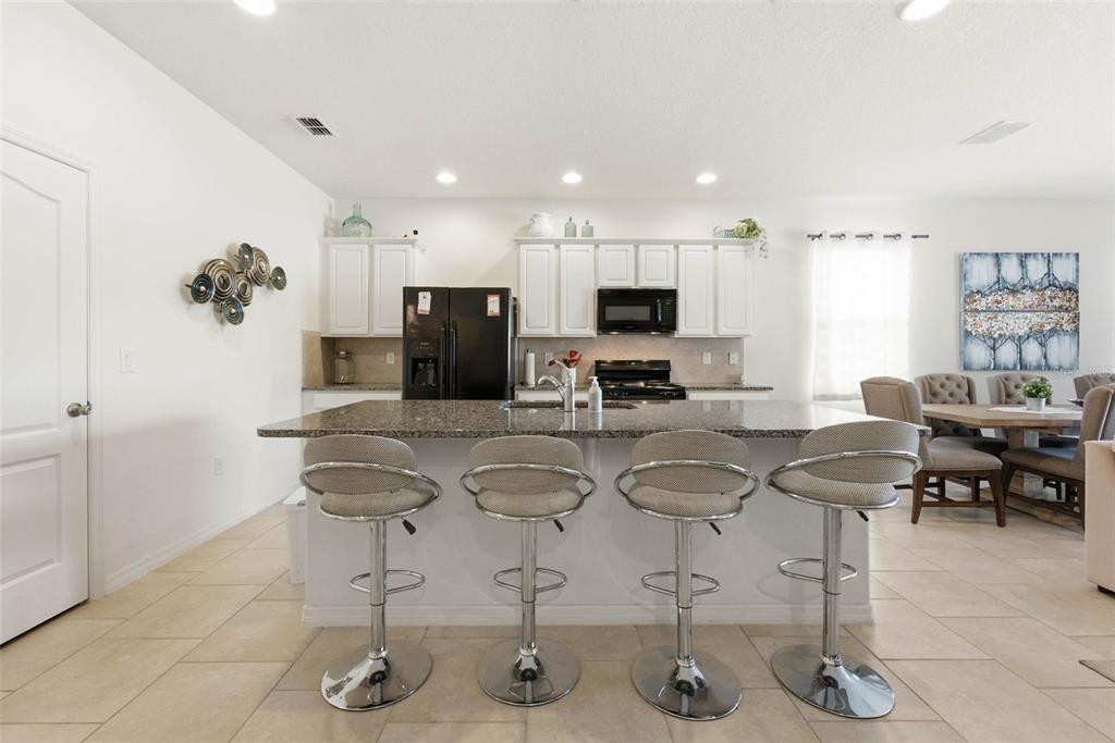A kitchen features a granite-topped island with four bar stools and white cabinetry — 4702 TERRASONESTA DRIVE, DAVENPORT, FL