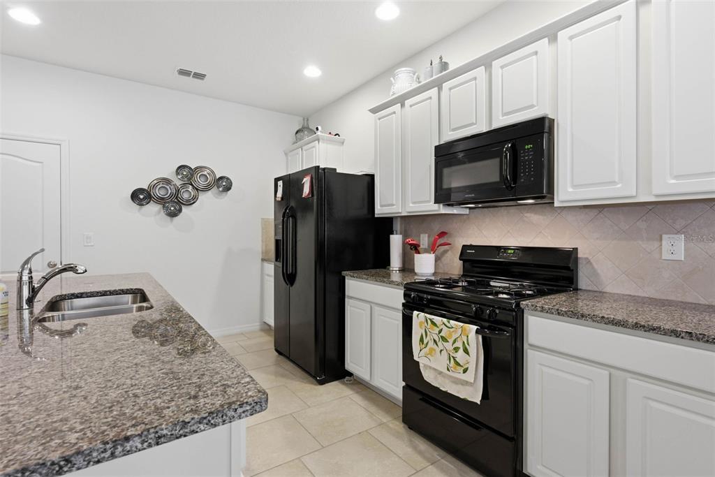 A kitchen features white cabinets, black appliances, granite countertops, and a central island with sink — 4702 TERRASONESTA DRIVE, DAVENPORT, FL