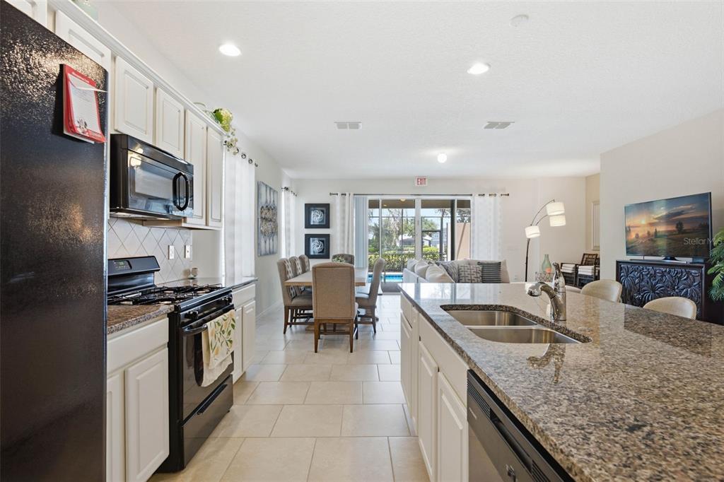 A kitchen with granite countertops and white cabinets opens into a dining and living area — 4702 TERRASONESTA DRIVE, DAVENPORT, FL