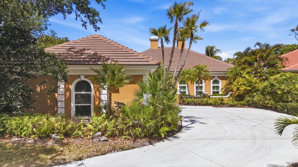 A tan house with a brown tile roof features a large concrete driveway and landscaping — 84 CAYMAN ISLES BOULEVARD, ENGLEWOOD, FL