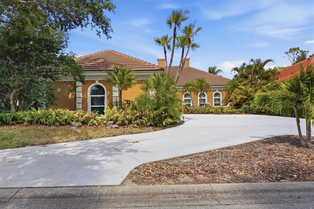 A single-story house with a tan stucco exterior, tile roof, and a curved concrete driveway — 84 CAYMAN ISLES BOULEVARD, ENGLEWOOD, FL