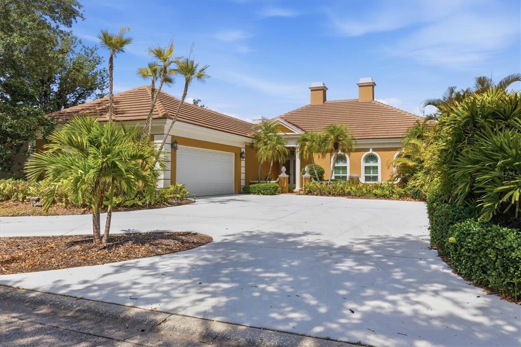 A single-story house with a tan exterior, tile roof, and a large concrete driveway — 84 CAYMAN ISLES BOULEVARD, ENGLEWOOD, FL