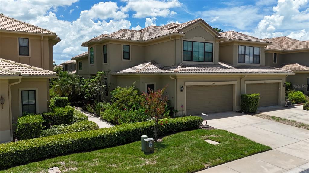 A two-story tan stucco townhouse with a tile roof, garage, and landscaped front yard — 8240 ACADIAN LANE, SEMINOLE, FL