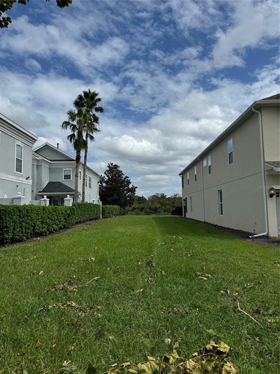 A grassy vacant lot sits between two multi-story residential houses under a cloudy sky — 7632 EXCITEMENT DRIVE, REUNION, FL
