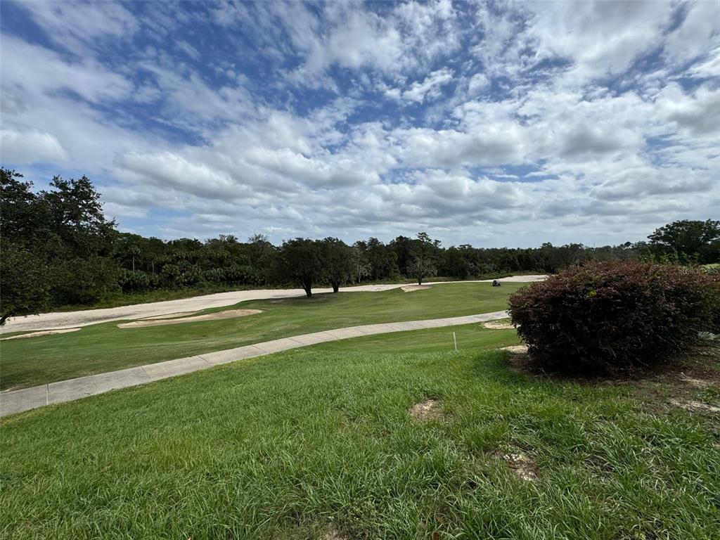 A view of a golf course fairway with a sand bunker and a paved path — 7632 EXCITEMENT DRIVE, REUNION, FL