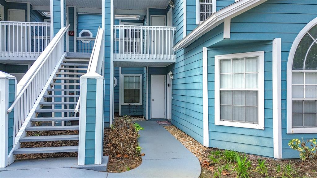 An exterior view of a blue apartment building with a staircase and a walkway — 8710 RAIN FOREST PLACE UNIT B, KISSIMMEE, FL