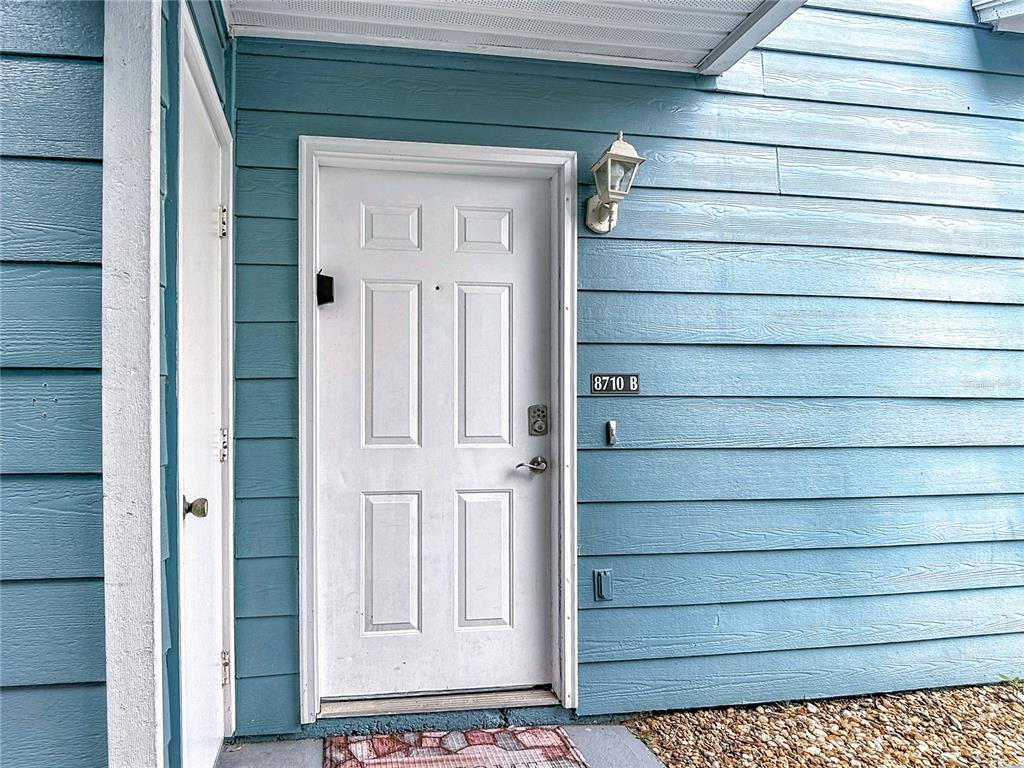 A white front door with a keypad lock is set against blue horizontal siding — 8710 RAIN FOREST PLACE UNIT B, KISSIMMEE, FL