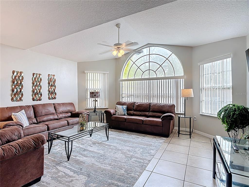 A living room features brown leather sofas, a glass coffee table, and a large arched window — 8710 RAIN FOREST PLACE UNIT B, KISSIMMEE, FL