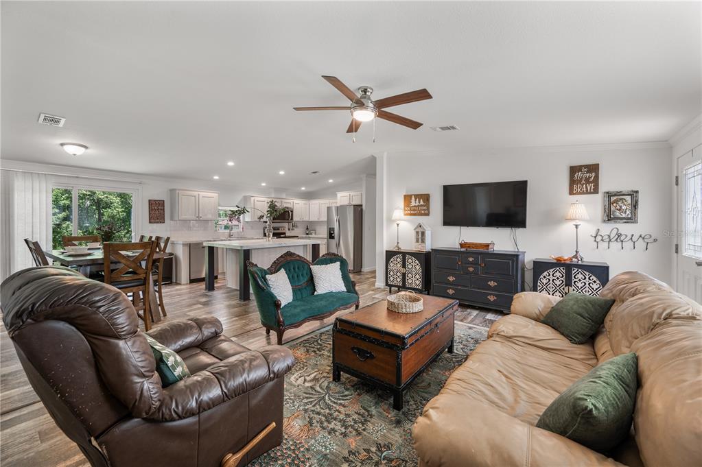 An open-concept living room and kitchen feature wood-look flooring, a ceiling fan, and neutral walls — 1321 WINDSONG DRIVE, LAKELAND, FL