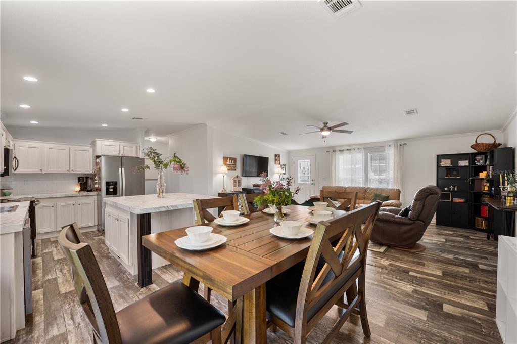 An open-concept kitchen and dining area features white cabinetry, a marble-topped island, and wood flooring — 1321 WINDSONG DRIVE, LAKELAND, FL
