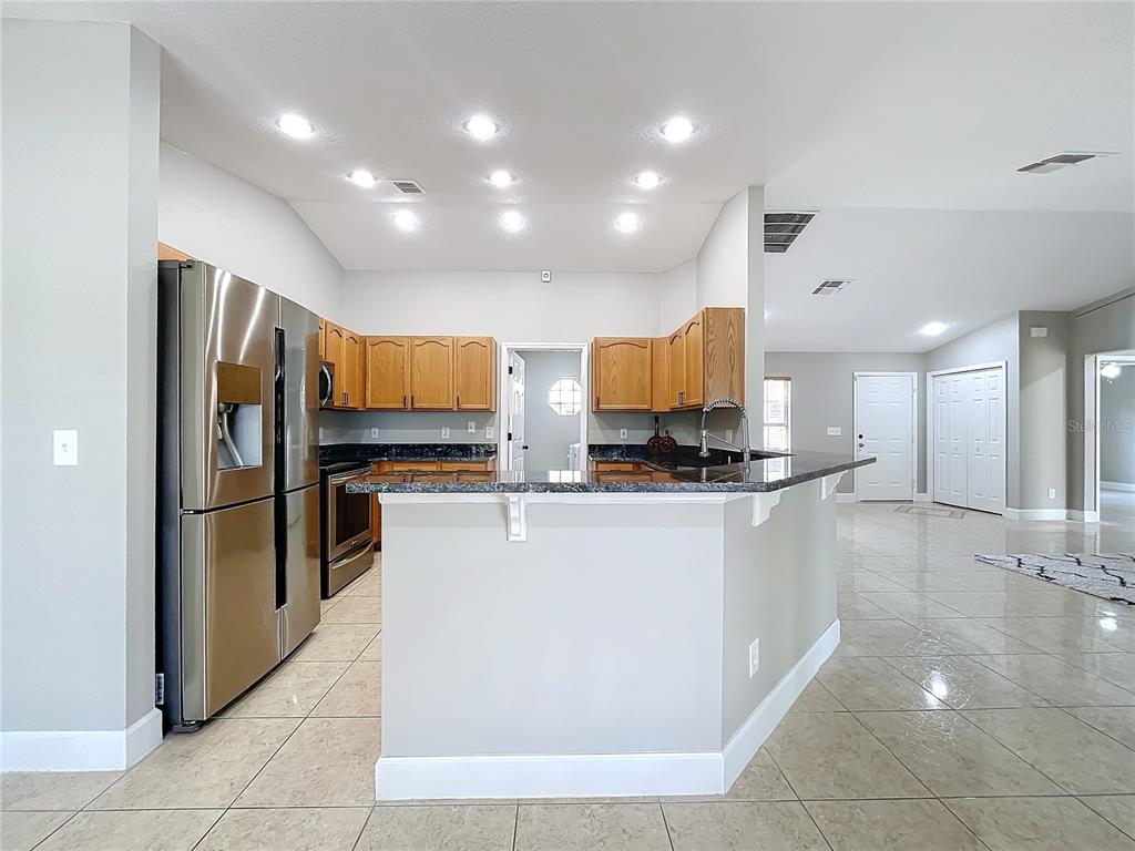 A kitchen with stainless steel appliances, wood cabinets, and a granite-topped peninsula island — 790 SILHOUETTE COURT, LONGWOOD, FL