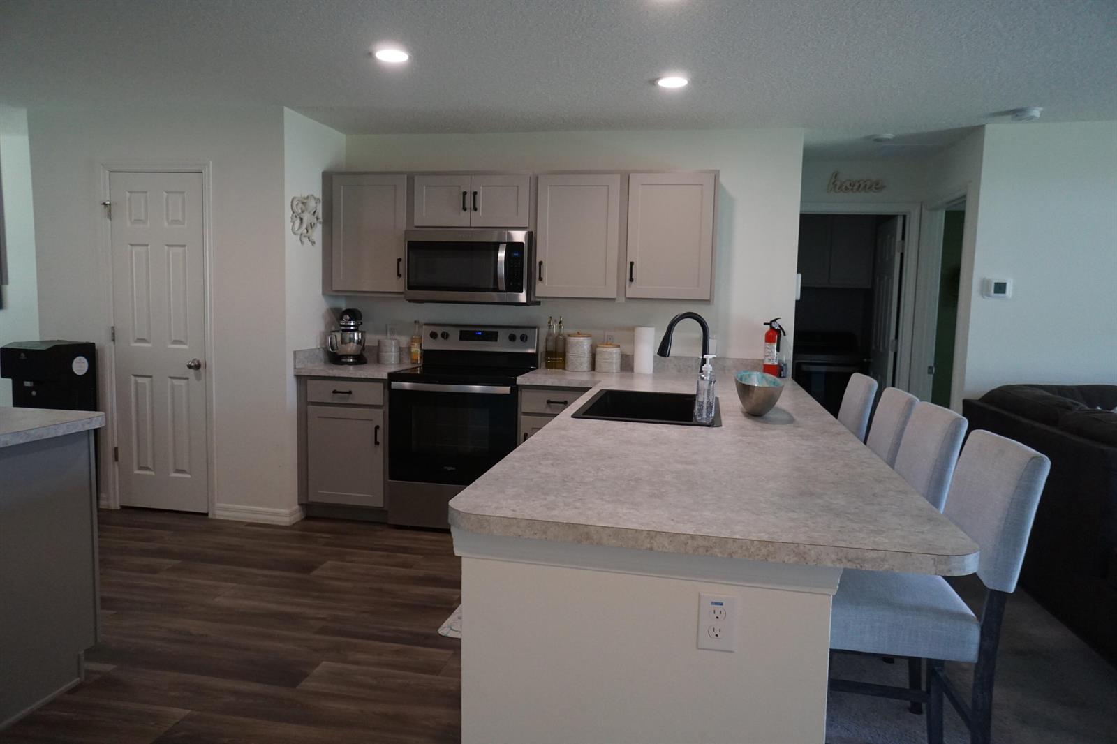 A kitchen features gray cabinets, stainless steel appliances, a large island, and wood-look flooring — 1014 Hammacher Avenue SW, Palm Bay FL 32908, PALM BAY, FL