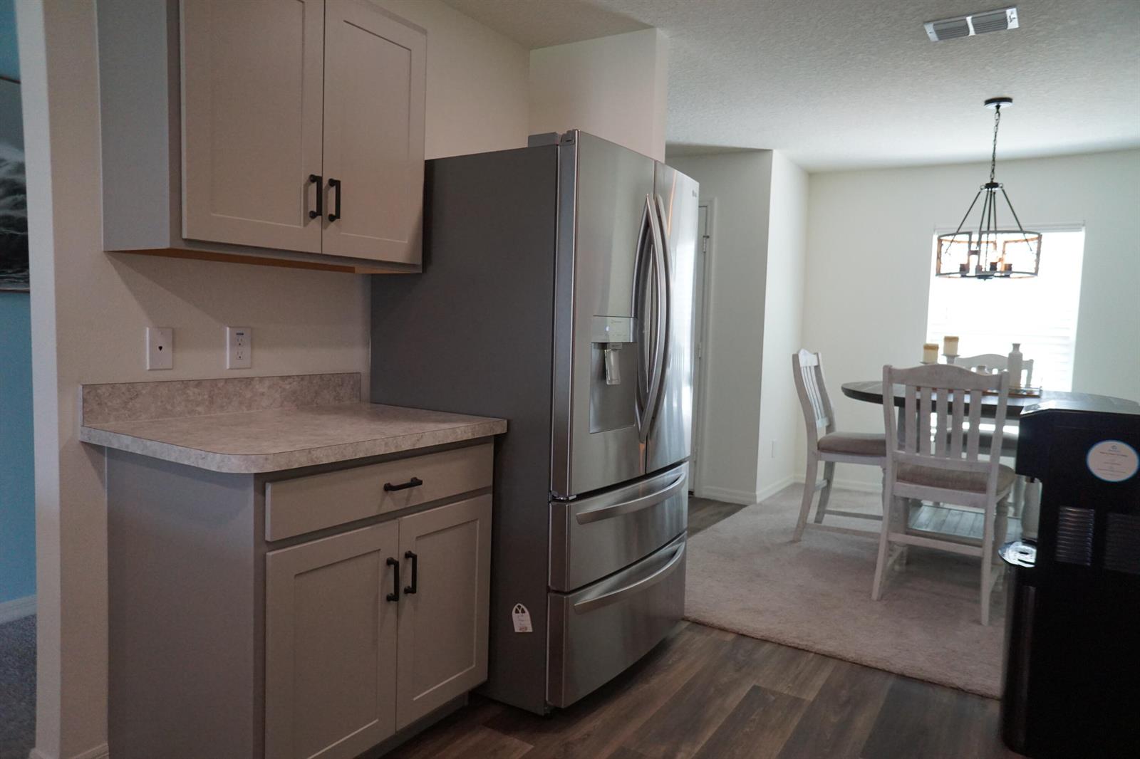 A kitchen features gray cabinets, a stainless steel refrigerator, and a dining area beyond — 1014 Hammacher Avenue SW, Palm Bay FL 32908, PALM BAY, FL