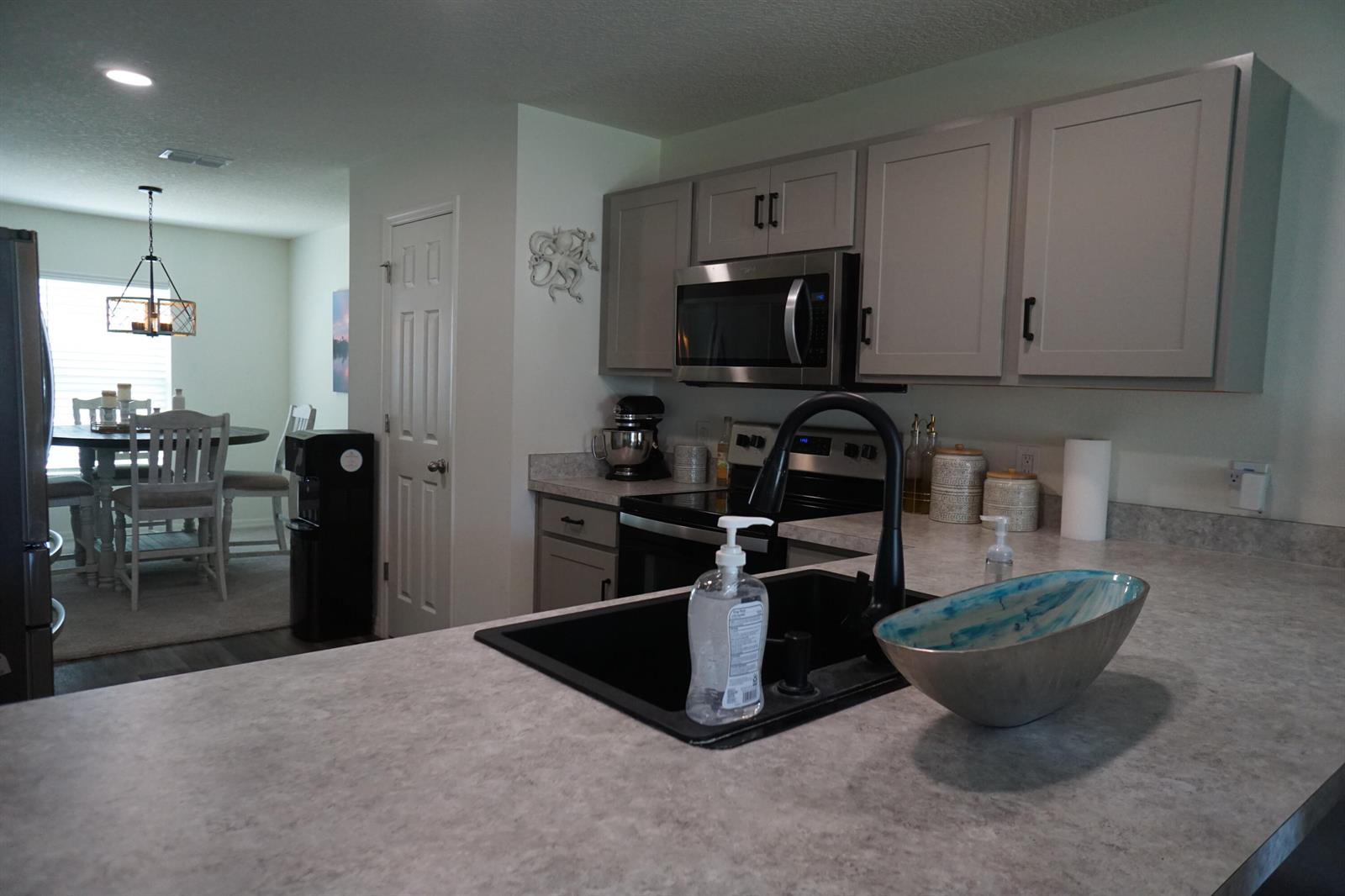 A kitchen features gray cabinets, a black sink, and a view into the dining area — 1014 Hammacher Avenue SW, Palm Bay FL 32908, PALM BAY, FL