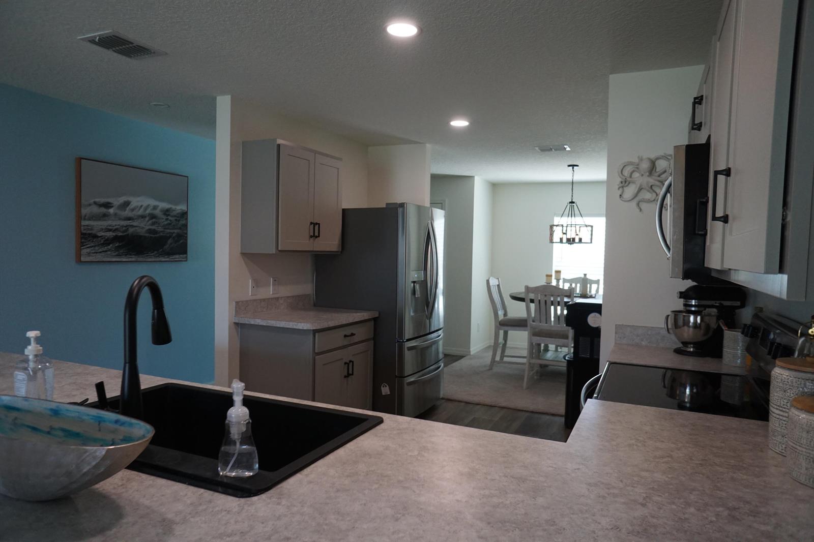 A kitchen with grey cabinets, stainless steel appliances, and a black sink overlooks a dining area — 1014 Hammacher Avenue SW, Palm Bay FL 32908, PALM BAY, FL