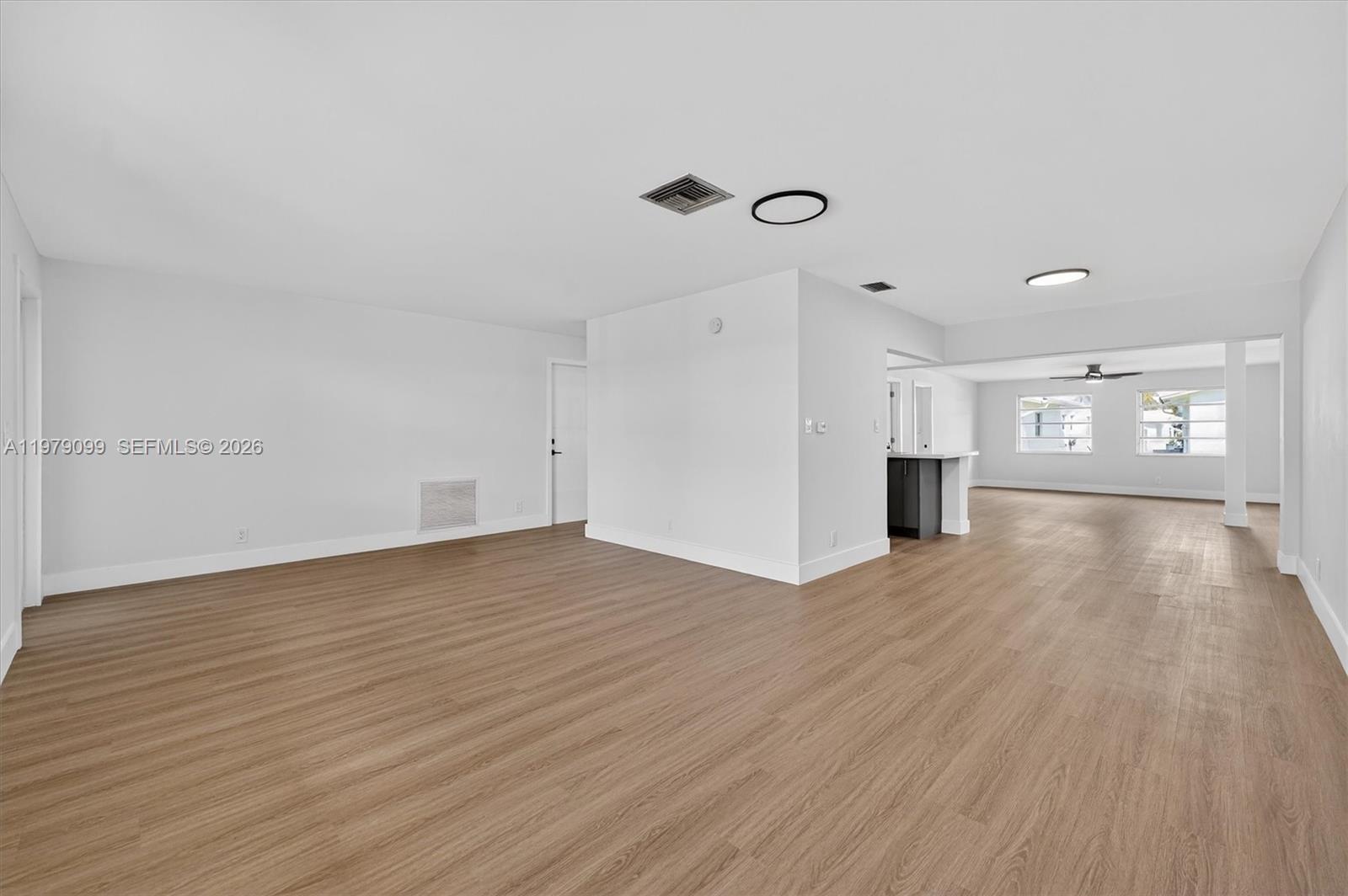 An open-concept living area features light wood-look flooring, white walls, and a central partition wall — 8941 NW 13th St, Plantation FL 33322, PLANTATION, FL