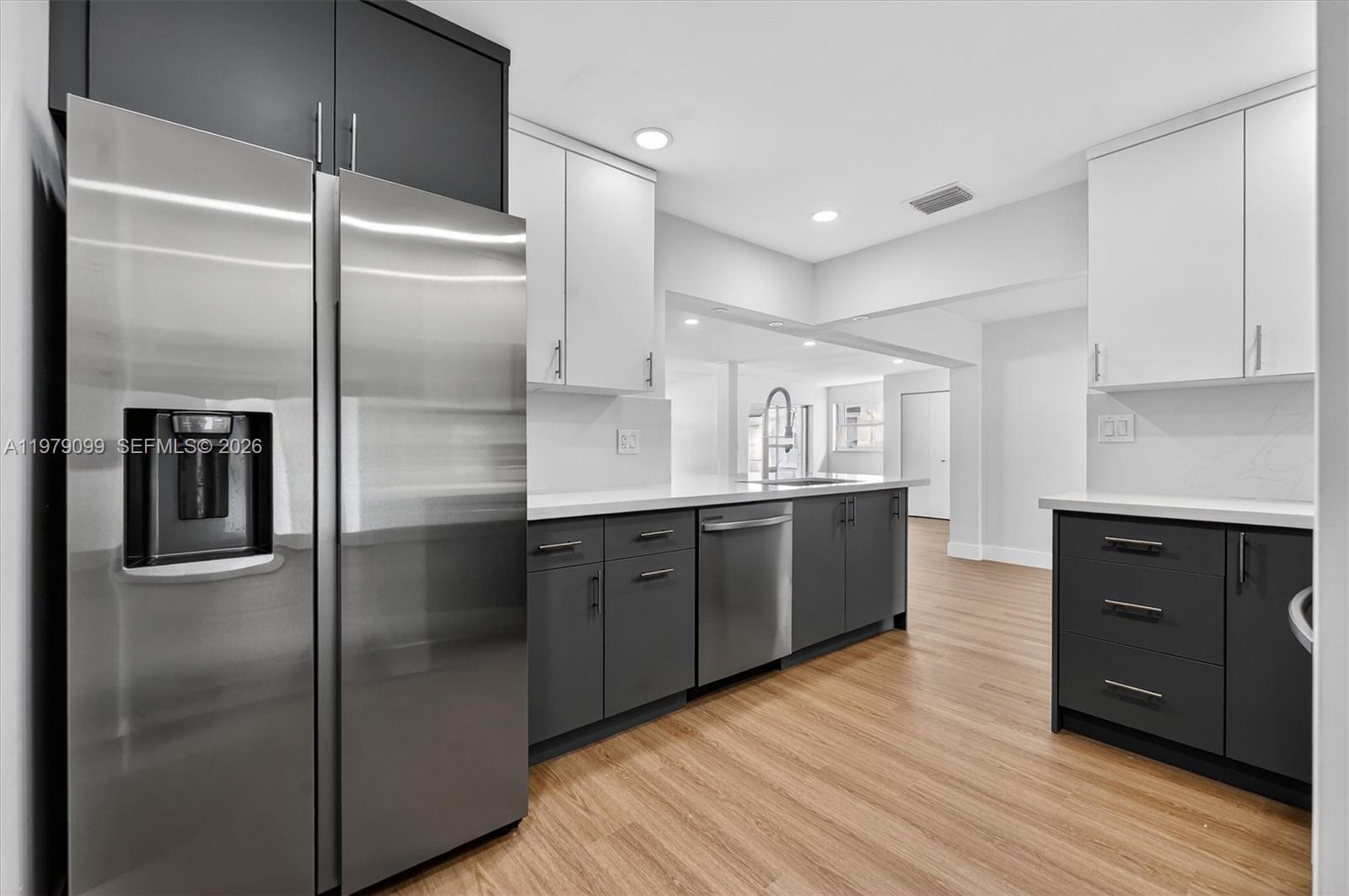 A modern kitchen features two-tone gray and white cabinetry, stainless steel appliances, and wood flooring — 8941 NW 13th St, Plantation FL 33322, PLANTATION, FL