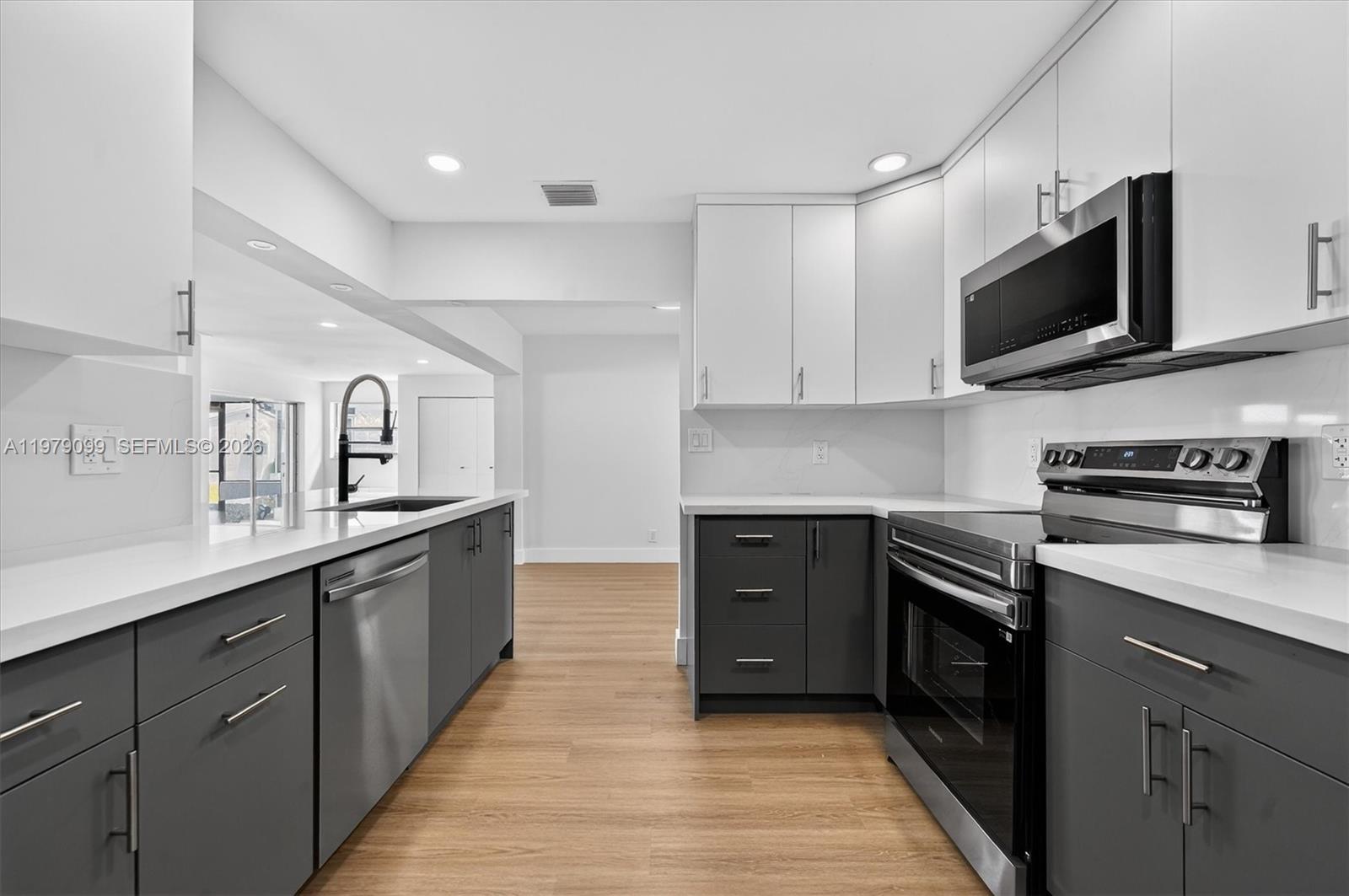 A modern kitchen features dark gray lower cabinets, white upper cabinets, and stainless steel appliances — 8941 NW 13th St, Plantation FL 33322, PLANTATION, FL