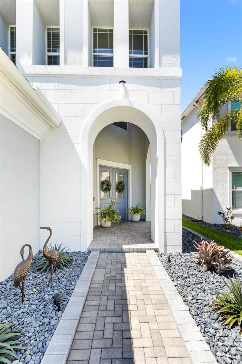 A white house exterior features an arched entryway with a paved walkway and gray doors — 16201 Melogold Drive, Westlake FL 33470, WESTLAKE, FL