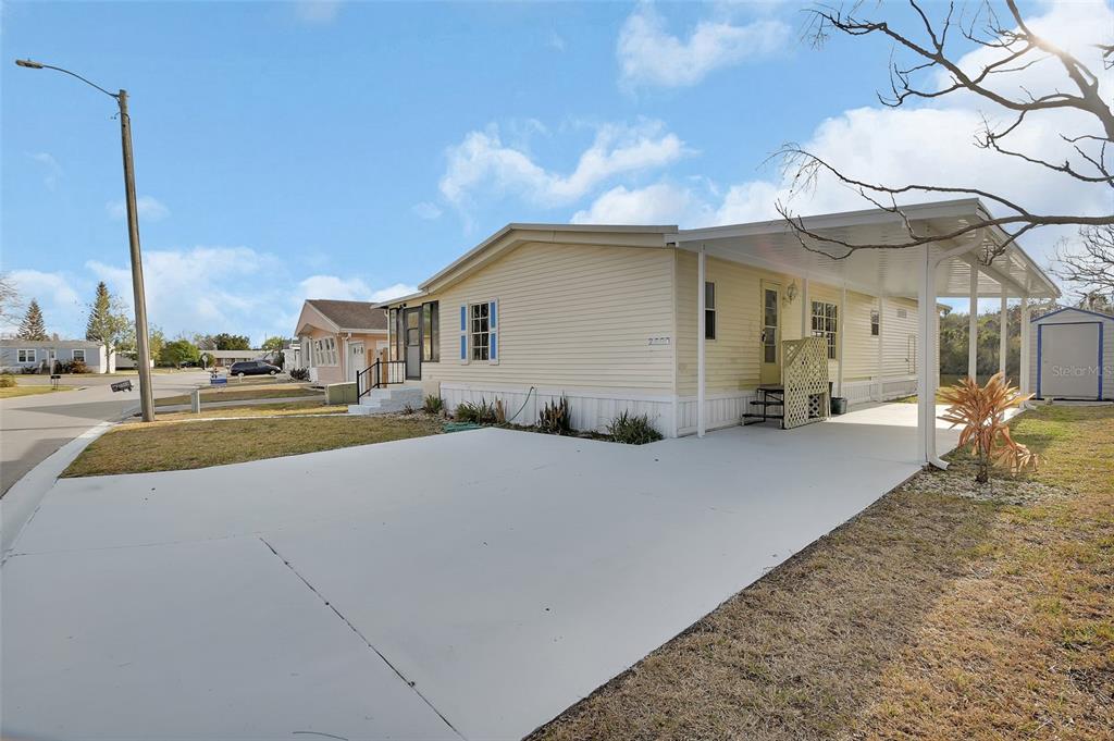A light yellow manufactured home features a covered carport, a concrete driveway, and a storage shed — 2008 HICKORYWOOD DRIVE, SOUTH DAYTONA, FL