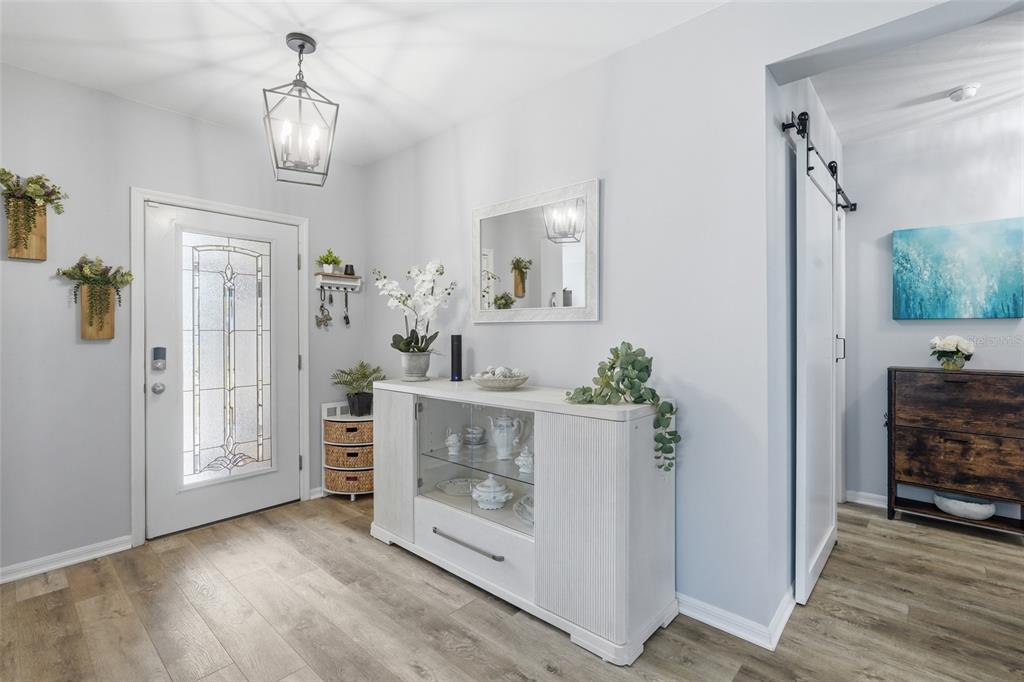 A bright entryway features a white front door, a glass-front console table, and wood-look flooring — 7081 WATERFORD PARKWAY, PUNTA GORDA, FL