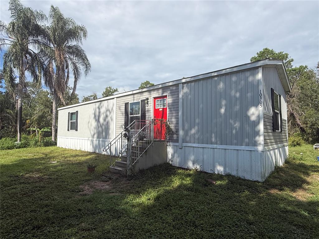 A single-story manufactured home with light gray siding and a bright red front door — 10305 REVELL ROAD, PARRISH, FL