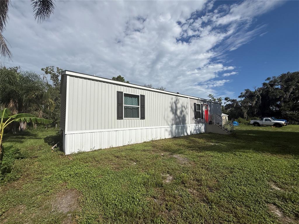 A side view of a light-colored mobile home with a red door and metal stairs — 10305 REVELL ROAD, PARRISH, FL
