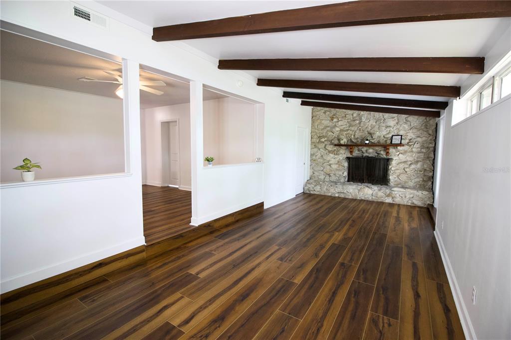 A living room features wood-look flooring, exposed ceiling beams, and a stone fireplace — 1114 OAK DRIVE, LEESBURG, FL