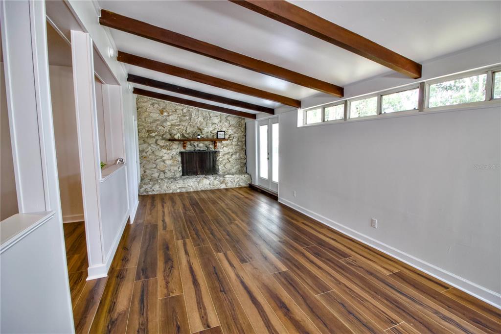 A living room features wood-look flooring, exposed ceiling beams, and a stone fireplace — 1114 OAK DRIVE, LEESBURG, FL