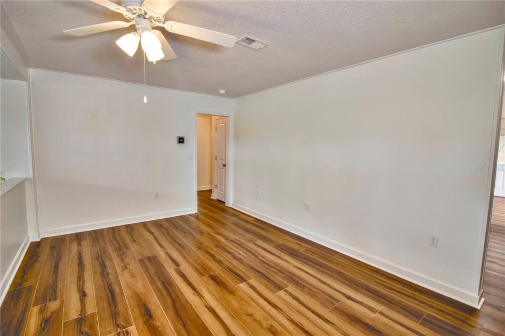An empty room features wood-look flooring, white walls, and a ceiling fan — 1114 OAK DRIVE, LEESBURG, FL
