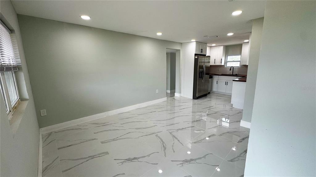 A room with light gray walls, white marble-patterned tile flooring, and an open kitchen area — 130 VIRGINIA COURT, ENGLEWOOD, FL