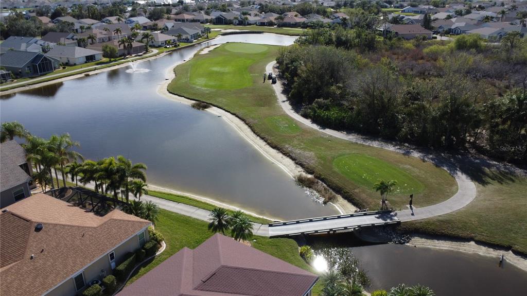An aerial view shows a golf course hole with a pond, bridge, and surrounding houses — 24327 BUCKINGHAM WAY, PUNTA GORDA, FL