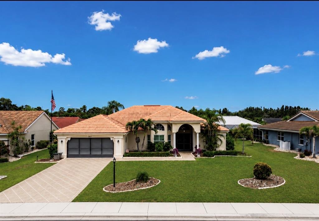 A single-story house with a tiled roof, garage, and front lawn under a blue sky — 2027 NEW BEDFORD DRIVE, SUN CITY CENTER, FL