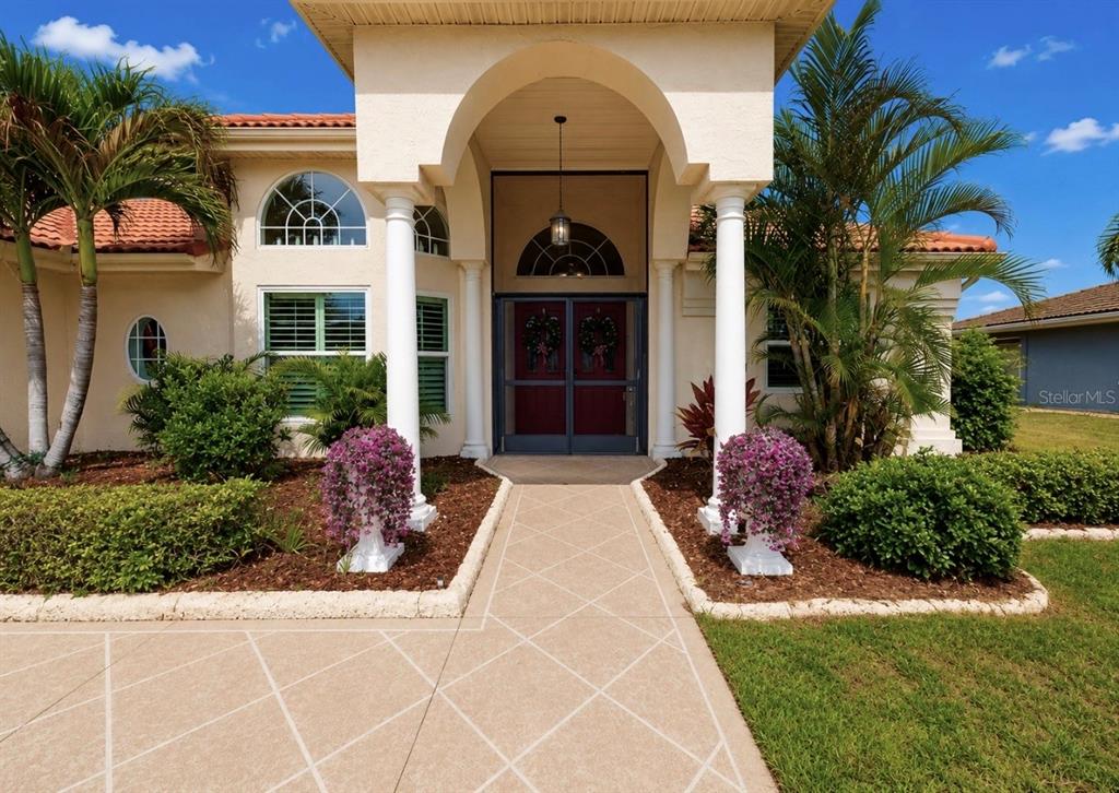 A front entrance features a covered porch with white columns, a walkway, and potted flowers — 2027 NEW BEDFORD DRIVE, SUN CITY CENTER, FL
