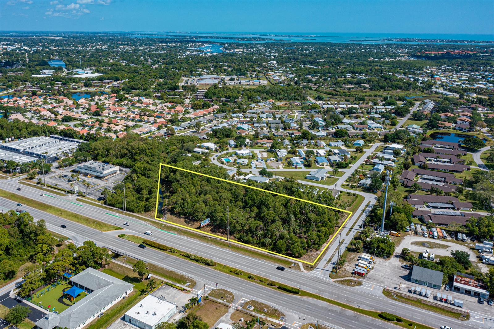 An aerial view shows a rectangular, tree-covered vacant lot outlined in yellow beside a highway — 0 SE Federal Highway, Stuart FL 34997, STUART, FL