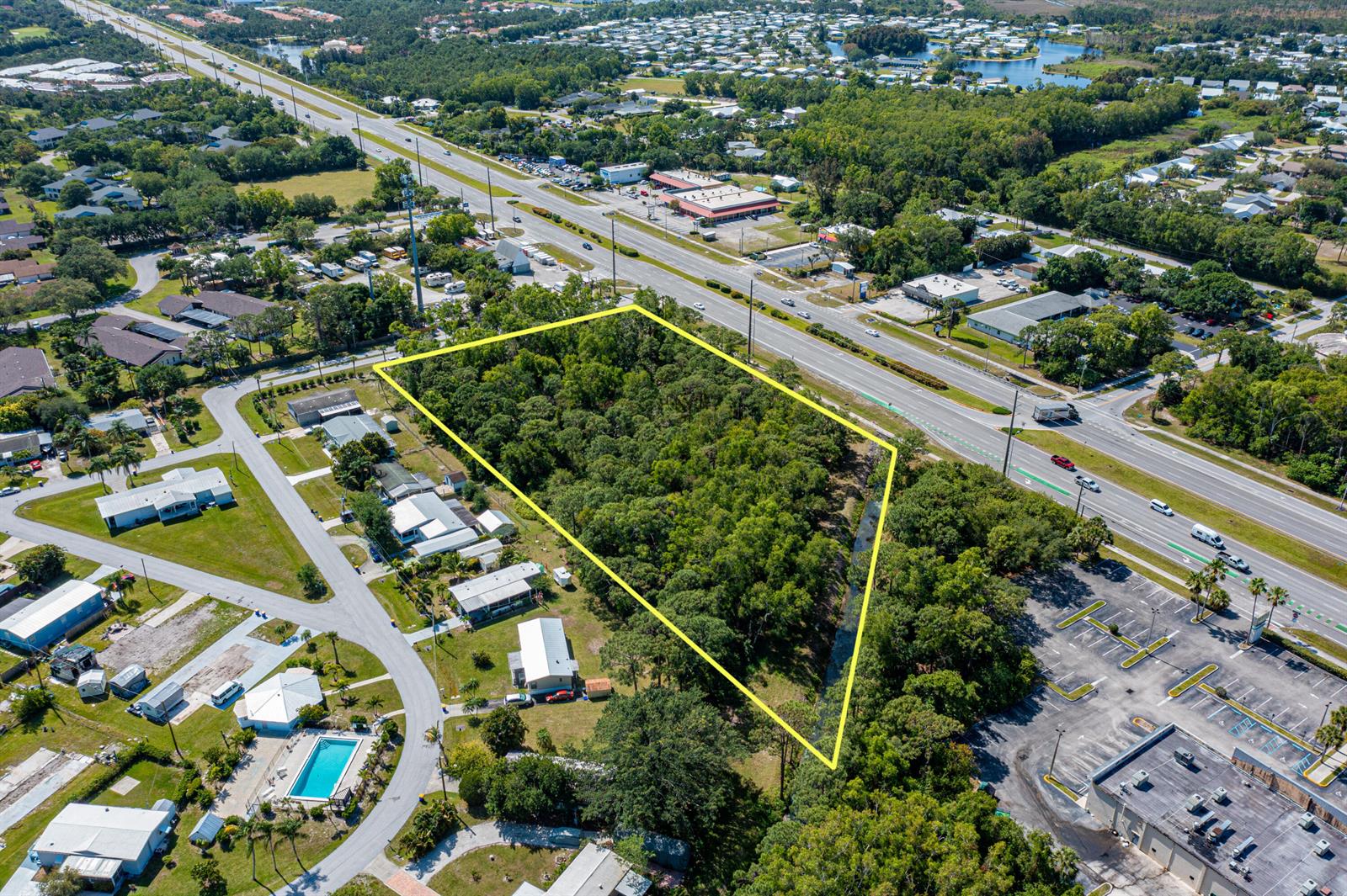 An aerial view shows a wooded, trapezoidal plot of land bordered by a road and buildings — 0 SE Federal Highway, Stuart FL 34997, STUART, FL