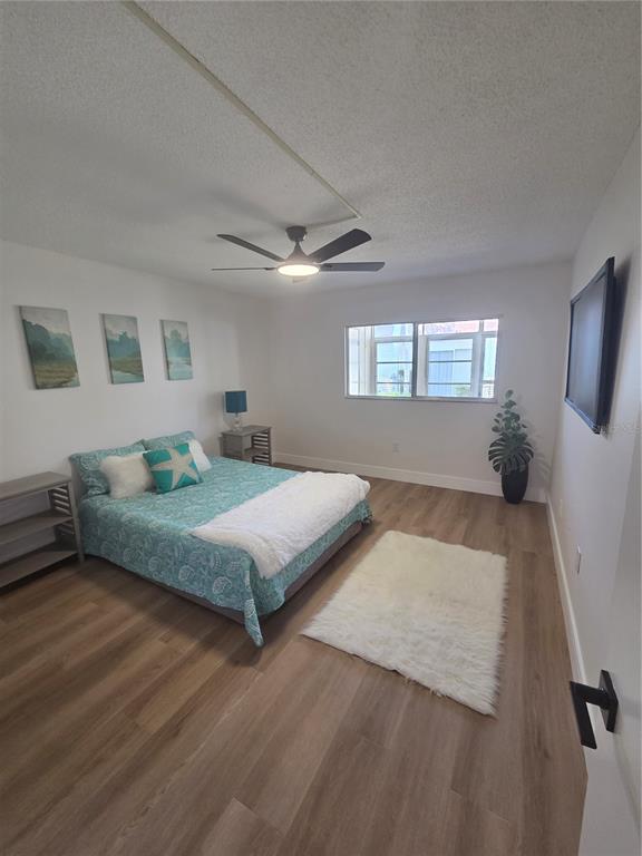 A bedroom features light wood flooring, a ceiling fan, a bed with teal bedding, and windows — 13719 MISSION OAKS BOULEVARD, SEMINOLE, FL