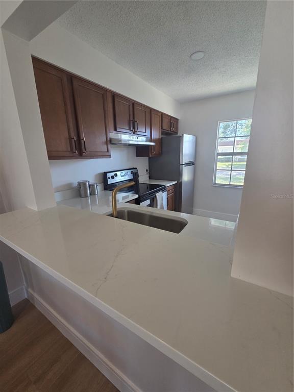 A kitchen features wood cabinets, stainless steel appliances, and a white quartz breakfast bar — 13719 MISSION OAKS BOULEVARD, SEMINOLE, FL
