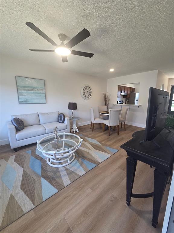 A living room with light wood flooring, a sofa, a dining set, and a ceiling fan — 13719 MISSION OAKS BOULEVARD, SEMINOLE, FL