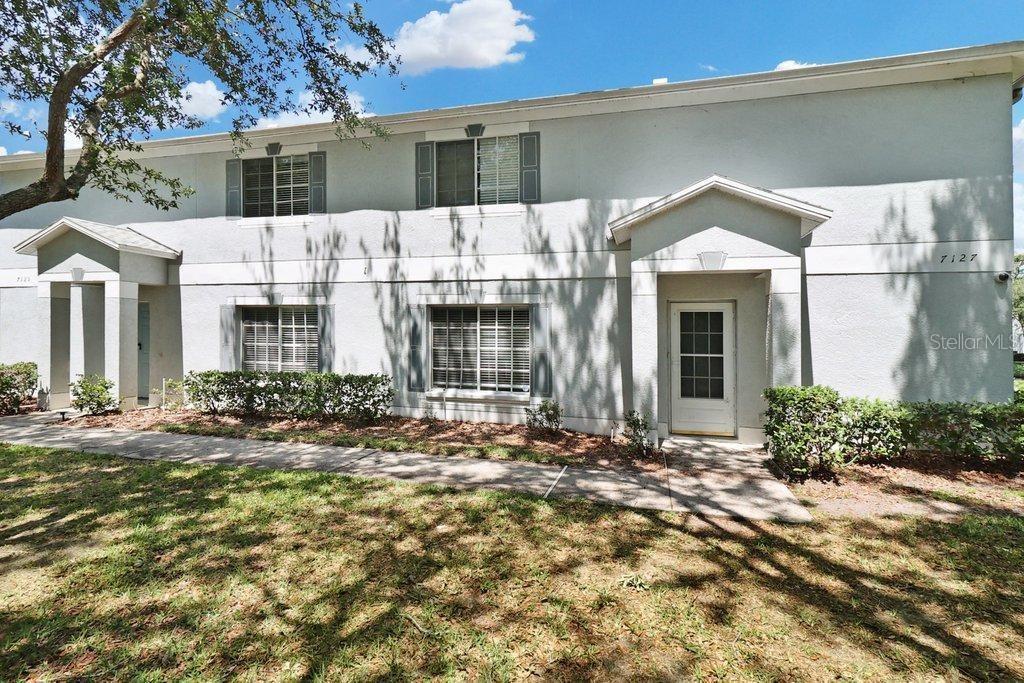 A two-story residential building with light-colored stucco walls, shuttered windows, and a covered entryway — 7127 WATERSIDE DRIVE, TAMPA, FL