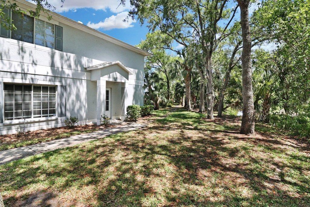 A two-story light-colored building with a front entrance sits beside a wooded, grassy area — 7127 WATERSIDE DRIVE, TAMPA, FL