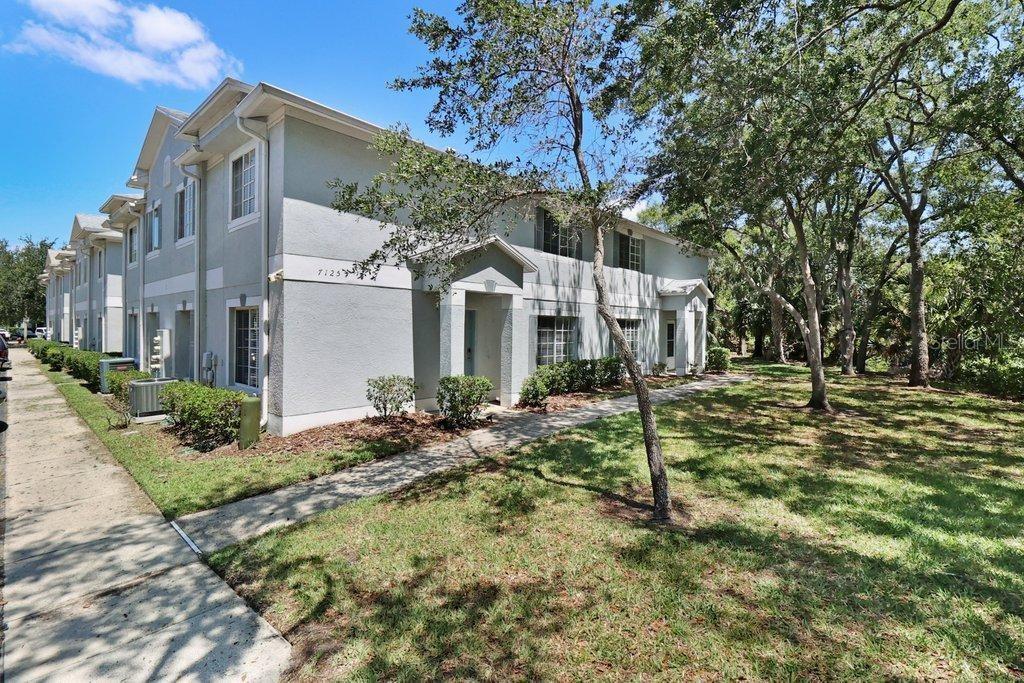 A two-story light-colored apartment building stands next to a sidewalk and a grassy area — 7127 WATERSIDE DRIVE, TAMPA, FL