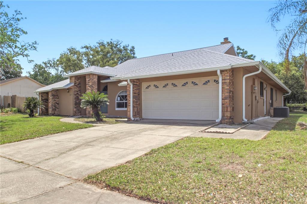 A single-story house with a tan stucco exterior, brick accents, and a two-car garage — 4649 CREEKVIEW LANE, OVIEDO, FL