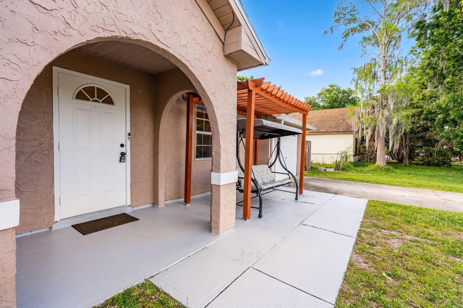 A tan stucco house features an arched entryway, a white front door, and a wooden pergola — 950 SE Taft Ave Avenue, Palm Bay FL 32909, PALM BAY, FL