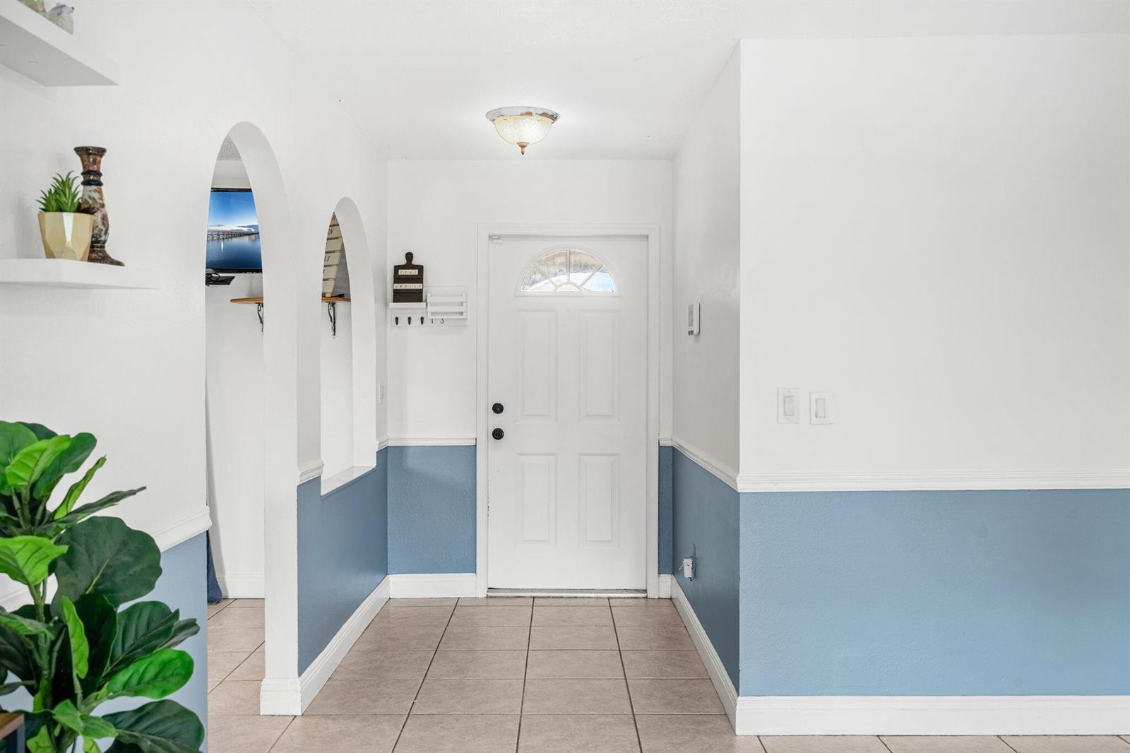 An entryway features a white door, tiled floors, and walls with blue wainscoting and arches — 950 SE Taft Ave Avenue, Palm Bay FL 32909, PALM BAY, FL